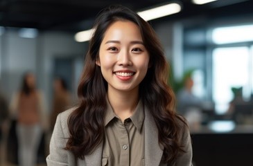 A smiling young graduate standing in an office with coworkers sitting by desks in the background.