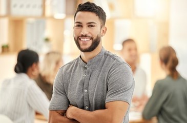 A graduate intern in an office space smiling at the camera with a team of professionals sitting around a table in the background.