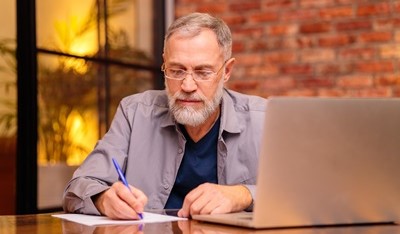 online-project-platform-for-education-providers A university supervisor making notes whilst sitting in an office by an open laptop.
